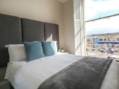 A bedroom with a bed with blue pillows and a gray headboard next to a window with shutters at The Esplanade in Weymouth