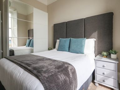 A bedroom with a double bed blue pillows a gray throw blanket a gray headboard and a white nightstand with decorations at The Esplanade in Weymouth