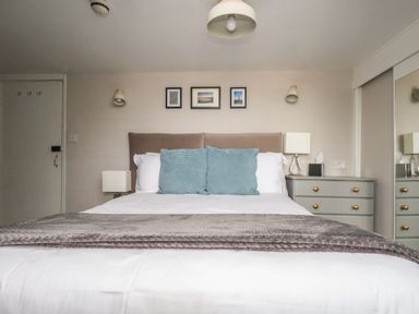 A bedroom with a bed with blue pillows and gray blanket bedside tables with lamps and framed pictures on the wall at The Esplanade in Weymouth