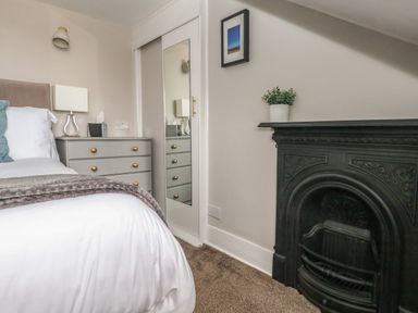 A bedroom with a bed white bedding a grey dresser a mirror on a closet door and a black fireplace at The Esplanade in Weymouth