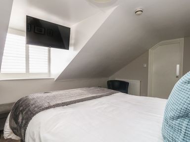 A bedroom with a bed a wall-mounted television a window with blinds a chair and a door at The Esplanade in Weymouth
