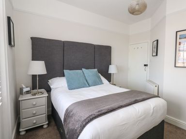 A bedroom with a double bed with grey headboard and blue cushions bedside tables with lamps and framed pictures on walls at The Esplanade in Weymouth