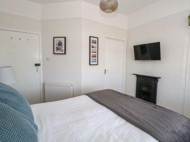 A bedroom with a bed covered in white sheets and gray blanket a wall-mounted TV above a fireplace and framed pictures on the walls at The Esplanade in Weymouth