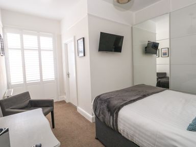 A bedroom with a bed a wall-mounted tv a chair a desk and mirrored wardrobe at The Esplanade in Weymouth