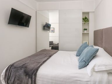 A bedroom with a bed with blue pillows and a gray blanket a wall-mounted TV and mirrored wardrobe at The Esplanade in Weymouth
