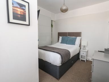 A bedroom with a bed with pillows and blanket a nightstand with a lamp a dresser and framed picture on the wall at The Esplanade in Weymouth
