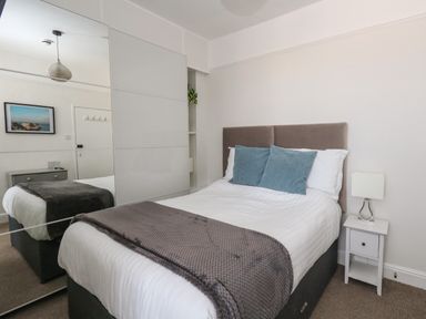 A bedroom with a bed two blue pillows and a gray blanket next to a nightstand with a lamp at The Esplanade in Weymouth