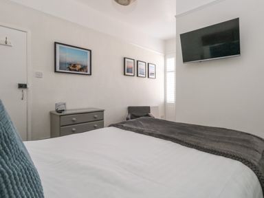 A bedroom with a bed a chest of drawers a chair wall art and a TV mounted on the wall at The Esplanade in Weymouth
