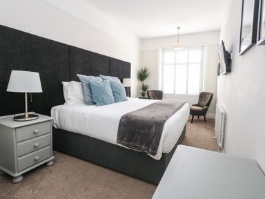A bedroom with a bed a nightstand with lamp two chairs and a plant near a window at The Esplanade in Weymouth