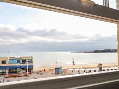 A view of the beach and sea with a building and beach huts visible through a window at The Esplanade in Weymouth