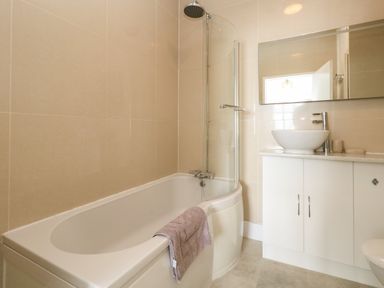 A bathroom with a bathtub shower combination a towel on the tub a sink with a countertop and cabinet below a large mirror on the wall at The Esplanade in Weymouth