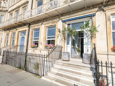 A building facade with stairs leading to a doorway flanked by two potted plants and window boxes with flowers at The Esplanade in Weymouth
