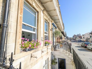 Street view of a row of buildings with flower boxes on windows and cars parked along the road at The Esplanade in Weymouth