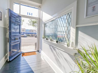 An open door with blue paint leading outside a hallway with small potted plants on a windowsill and a green plant in the corner at The Esplanade in Weymouth