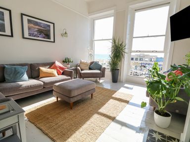 A living room with sofas cushions plants and large windows with a view at The Esplanade in Weymouth