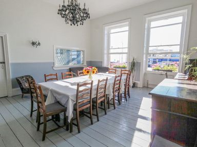 A dining room with a long table covered with a white tablecloth and wooden chairs around it at The Esplanade in Weymouth