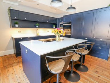 A kitchen with blue cabinets a marble island a vase of flowers and wooden floor at The Esplanade in Weymouth
