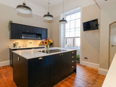 A kitchen with black cabinets a marble countertop an island with flowers a window and a wall-mounted TV at The Esplanade in Weymouth