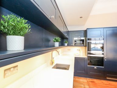 A kitchen with black cabinets white countertop a sink built in oven microwave and potted plants at The Esplanade in Weymouth
