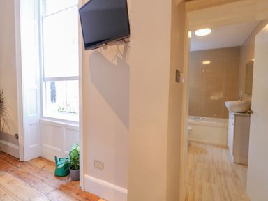A corner of a room with a wall-mounted television a window and plants next to an entrance leading to a bathroom at The Esplanade in Weymouth