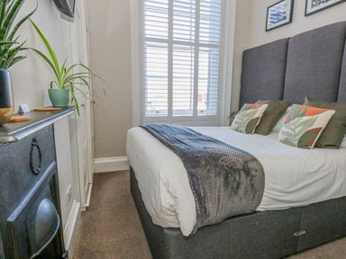 A bedroom with a bed planted against the wall with pillows and plants on a mantelpiece at The Esplanade Weymouth
