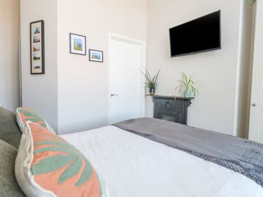A bedroom with a bed with pillows and a blanket a wall-mounted television and potted plants on a mantel at The Esplanade in Weymouth
