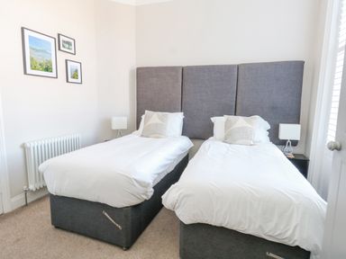 A bedroom with two single beds with gray headboards white bedding and framed pictures on the wall at The Esplanade in Weymouth