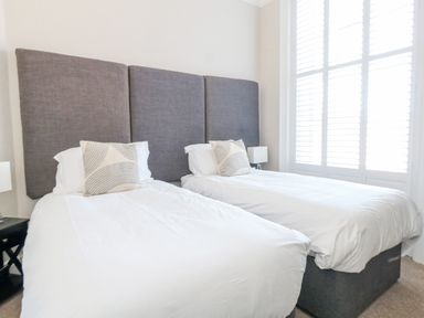 A bedroom with two single beds with gray headboards and white bedding at The Esplanade in Weymouth