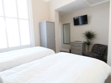 A bedroom with two beds a grey wardrobe a chest of drawers a wall-mounted TV a chair and a plant at The Esplanade in Weymouth