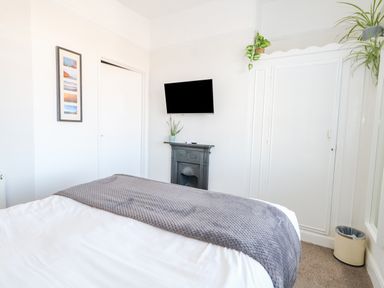 A bedroom with a bed covered by a gray blanket a wall-mounted television a small fireplace plants and a closet at The Esplanade in Weymouth