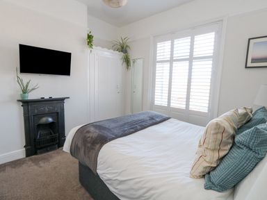 A bedroom with a bed near a window with shutters a wall-mounted television and a small fireplace at The Esplanade in Weymouth