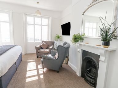 A bedroom with a bed two armchairs a fireplace with mirror and plants and a wall mounted tv at The Esplanade in Weymouth