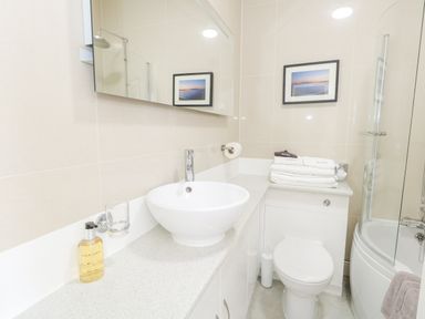 A bathroom with a round sink toilet towels and a bathtub with a glass shower screen at The Esplanade in Weymouth
