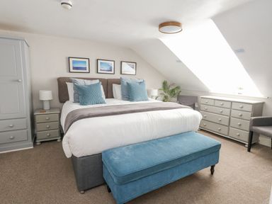 A bedroom with a double bed blue bench two armchairs gray dresser and wardrobe at The Esplanade in Weymouth