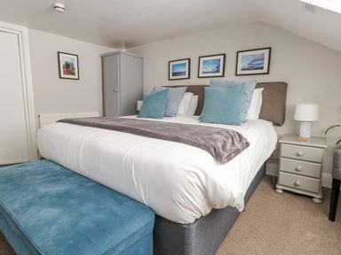A bedroom with a large bed blue cushions a blue bench bedside table with lamp wardrobe and framed pictures on the wall at The Esplanade in Weymouth