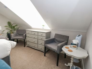 A bedroom corner with two grey armchairs a grey dresser a white side table with coasters and a tissue box and a potted plant at The Esplanade in Weymouth