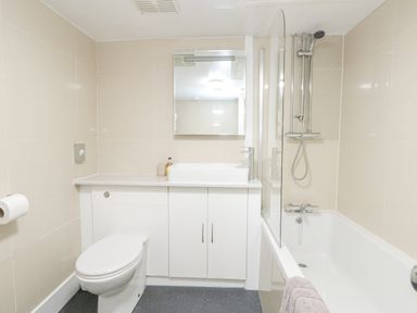 A bathroom with a toilet a sink with a mirror above and a bathtub with shower at The Esplanade Weymouth