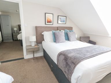 A bedroom with a double bed with pillows and a blanket a side table with a lamp and an armchair at The Esplanade in Weymouth