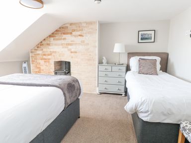 A bedroom with two single beds a gray chest of drawers a lamp and a brick fireplace at The Esplanade in Weymouth