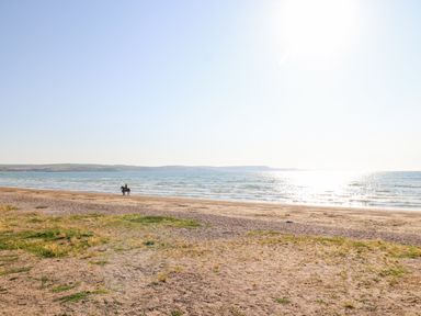 A beach with grass patches and a person riding a horse near the shoreline at The Esplanade in Weymouth