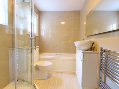 A bathroom with a shower, toilet, bathtub, sink with cabinet, mirror, and towel radiator at The Esplanade in Weymouth