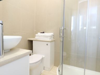 A bathroom with a toilet, sink, countertop, towels, and a glass shower at The Esplanade in Weymouth