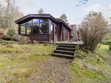 A wooden cabin with large glass windows and stone steps leading to a grassy area at Rocksite in Kirkmichael Perth And Kinross