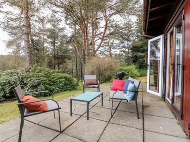 An outdoor patio with a glass table surrounded by three chairs with colorful cushions next to a wooden building at Rocksite in Kirkmichael Perth And Kinross