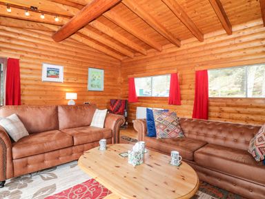 A living room with two brown sofas a wooden coffee table and red curtains at Rocksite in Kirkmichael Perth And Kinross