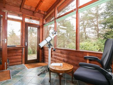 A wooden sunroom with a telescope by large windows a black office chair and a small round wooden table at Rocksite in Kirkmichael Perth And Kinross