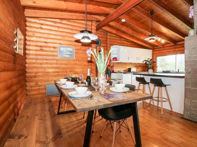 A dining area with a wooden table set with bowls glasses and cutlery next to a kitchen with white cabinets and black bar stools at Rocksite in Kirkmichael Perth And Kinross