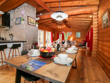 A dining table set with bowls, glasses, and a bowl of fruit in a wooden log cabin with a kitchen and living area at Rocksite Kirkmichael Perth And Kinross