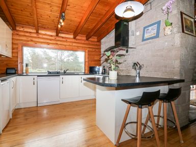 A kitchen with wooden ceiling and floor a countertop with two stools and a window overlooking trees at Rocksite Kirkmichael Perth And Kinross