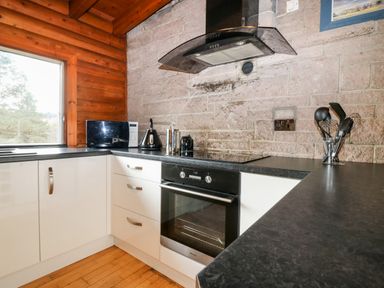 A kitchen with black countertops white cabinets a microwave kettle and cooking utensils at Rocksite Kirkmichael Perth And Kinross